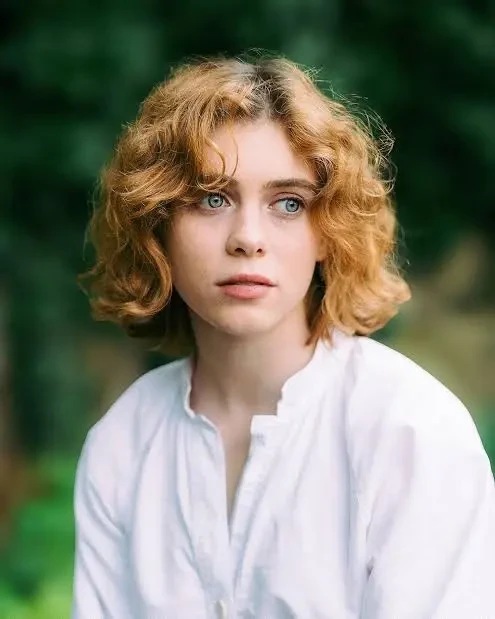 Retrato da atriz Sophia Lillis com cabelo curto ondulado e camisa branca, perante um fundo verde natural. A atriz integra o elenco principal do jogo OD Knock de Hideo Kojima.